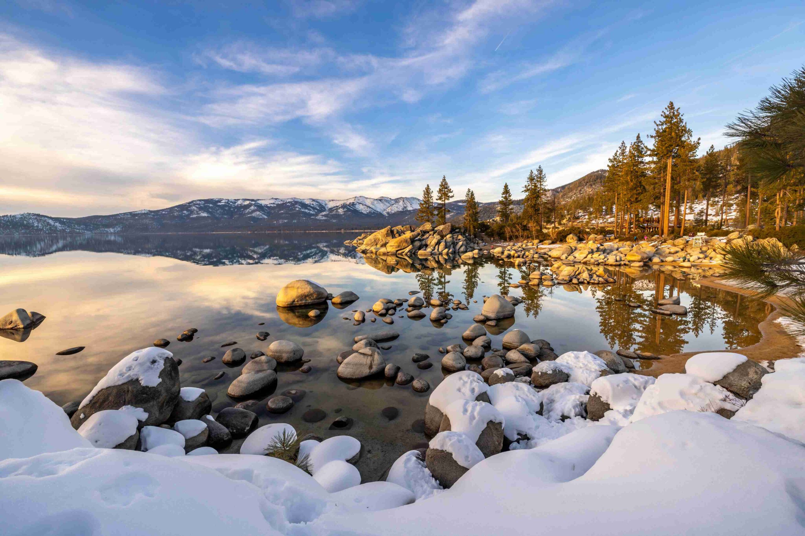 A still alpine lake framed by snow-dusted peaks and pines at golden hour